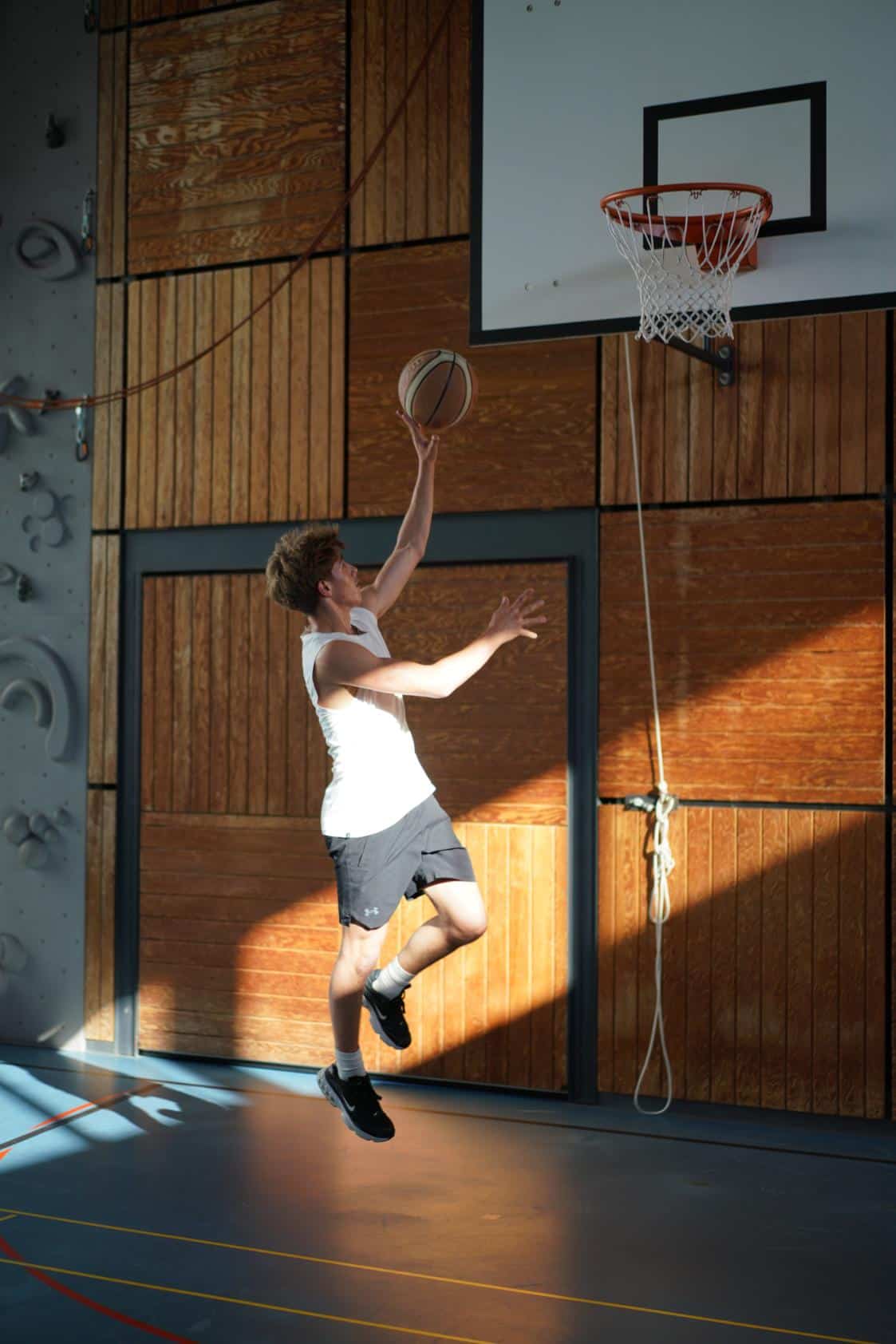 Young boy playing basketball indoors at school gymnasium.