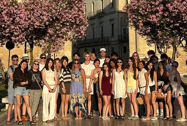 Diverse group of students standing outdoors with pink flowering trees in the background.