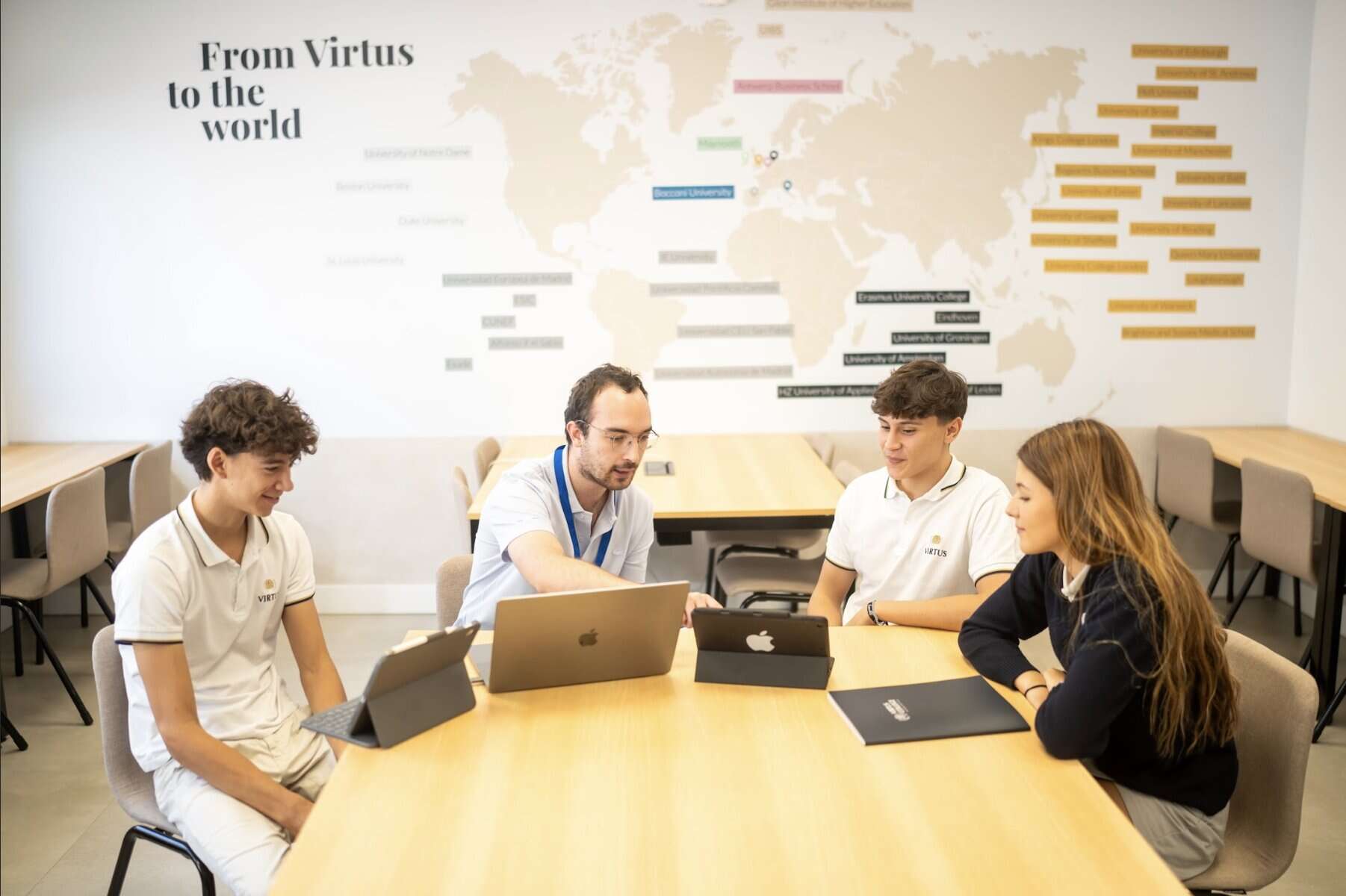 Group of diverse students and teacher discussing in classroom with world map.