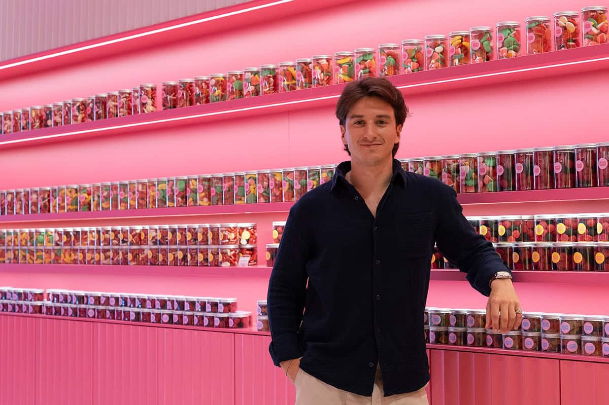 Young man standing in colorful candy store with pink walls and shelves of jars.